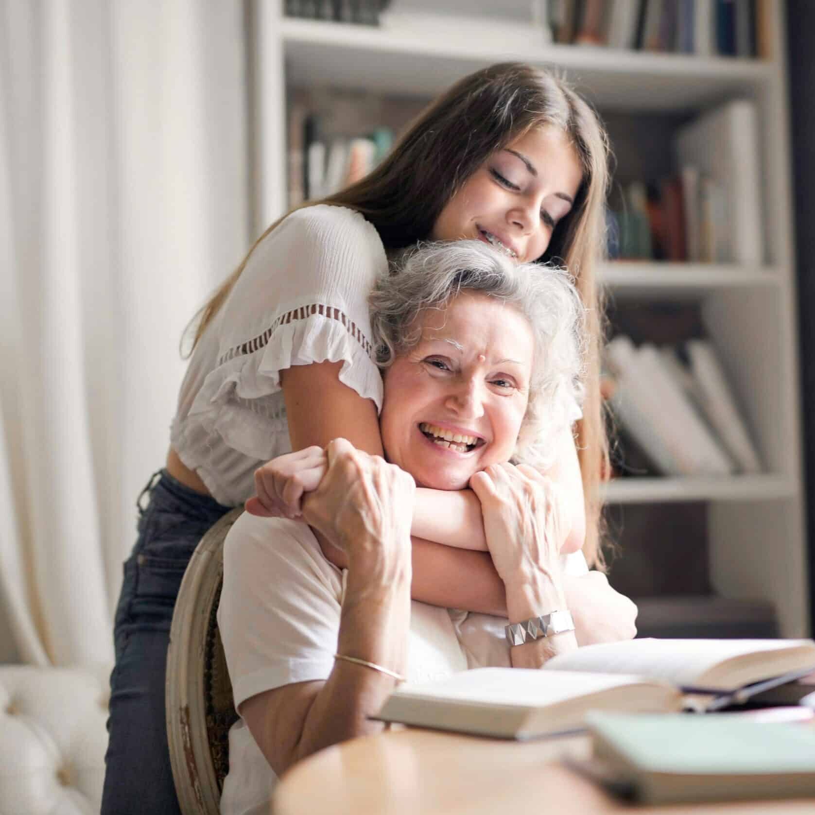 Older woman smiling with young girl hugging her from behind.